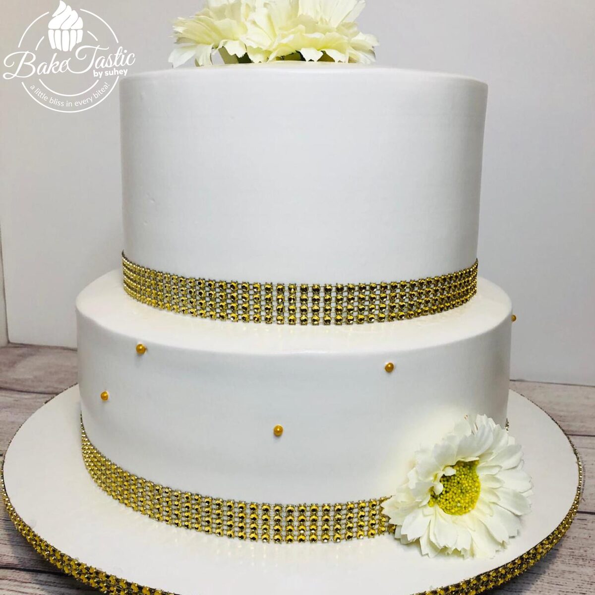 Two-tier white wedding cake with gold rhinestone bands and flowers